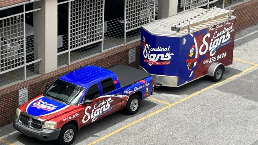 The Cardinal Signs wrapped work truck and trailer, both covered in the shop’s blue and red vehicle wrap